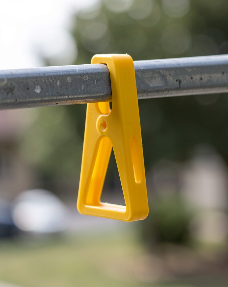 A blank yellow corrugated plastic strip clipped to a bare wooden rail on a lawn, unprinted side facing out, house curtains closed