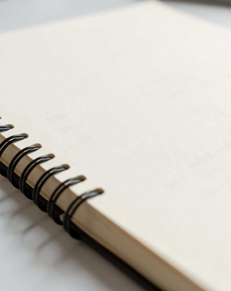 A closed report binder with a fabric bookmark ribbon on a kitchen table beside two coffee mugs