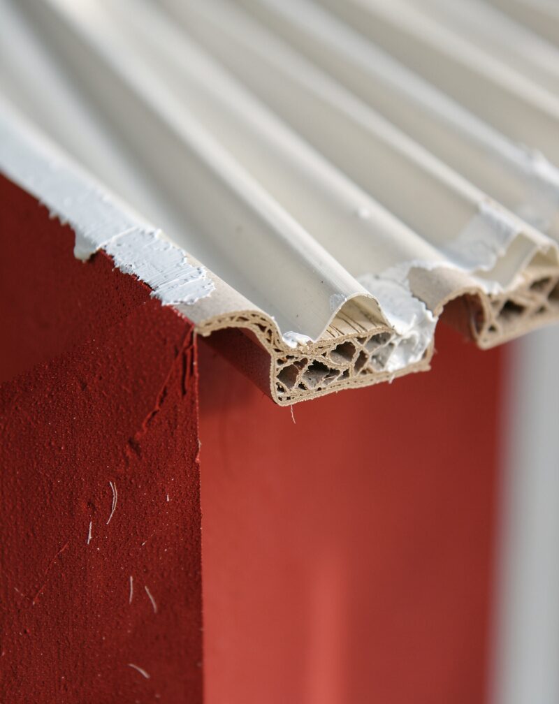 A red corrugated plastic sign panel lying flat on sawhorses in a garage workshop, a tin of white paint and a brush beside it