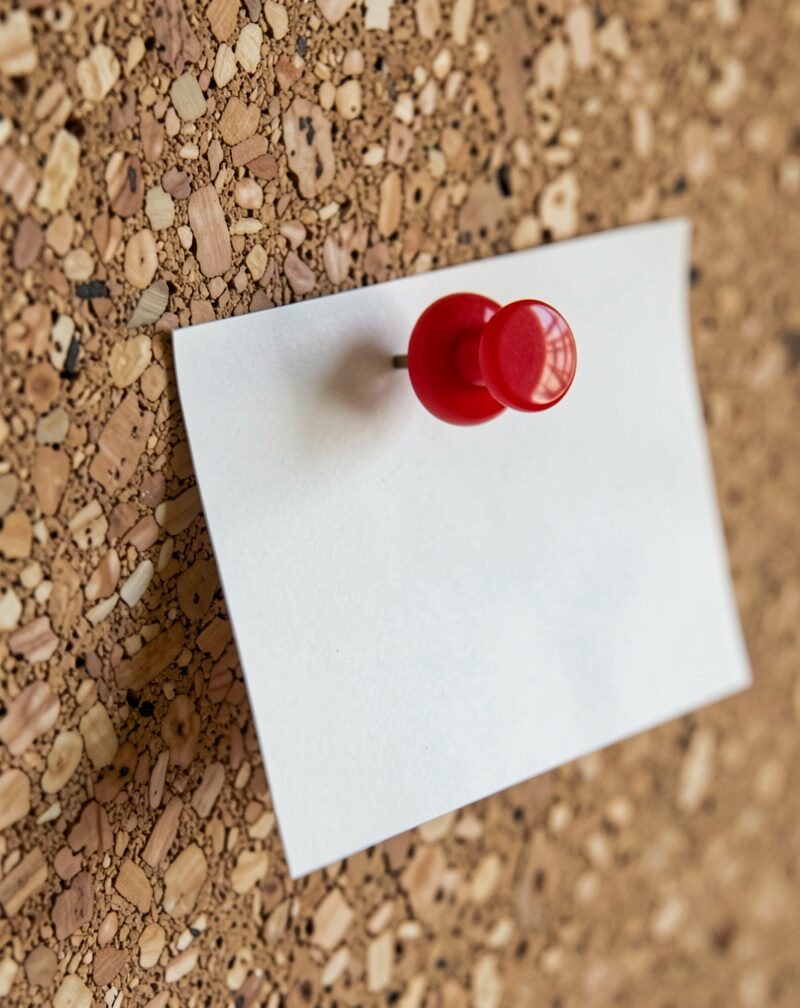 A paper map pinned printed-side to a corkboard so only its blank cream reverse faces the camera, pushpins at the corners